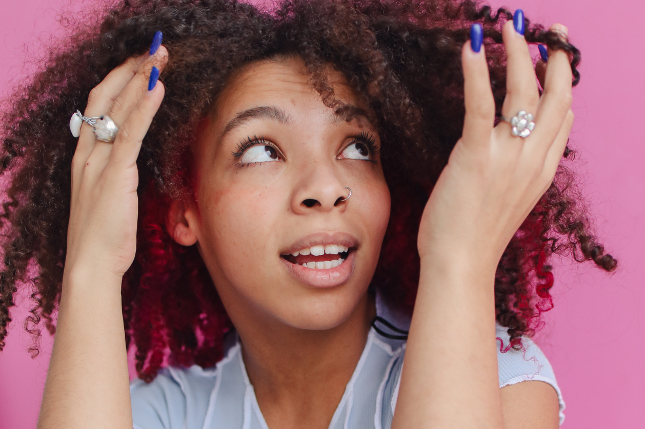 Woman examining her natural curls, representing hair porosity awareness and textured hair care.
