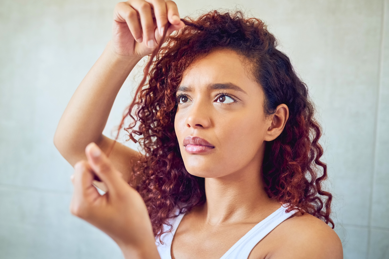 Woman examining her curly hair strand closely, noticing changes in hair texture.