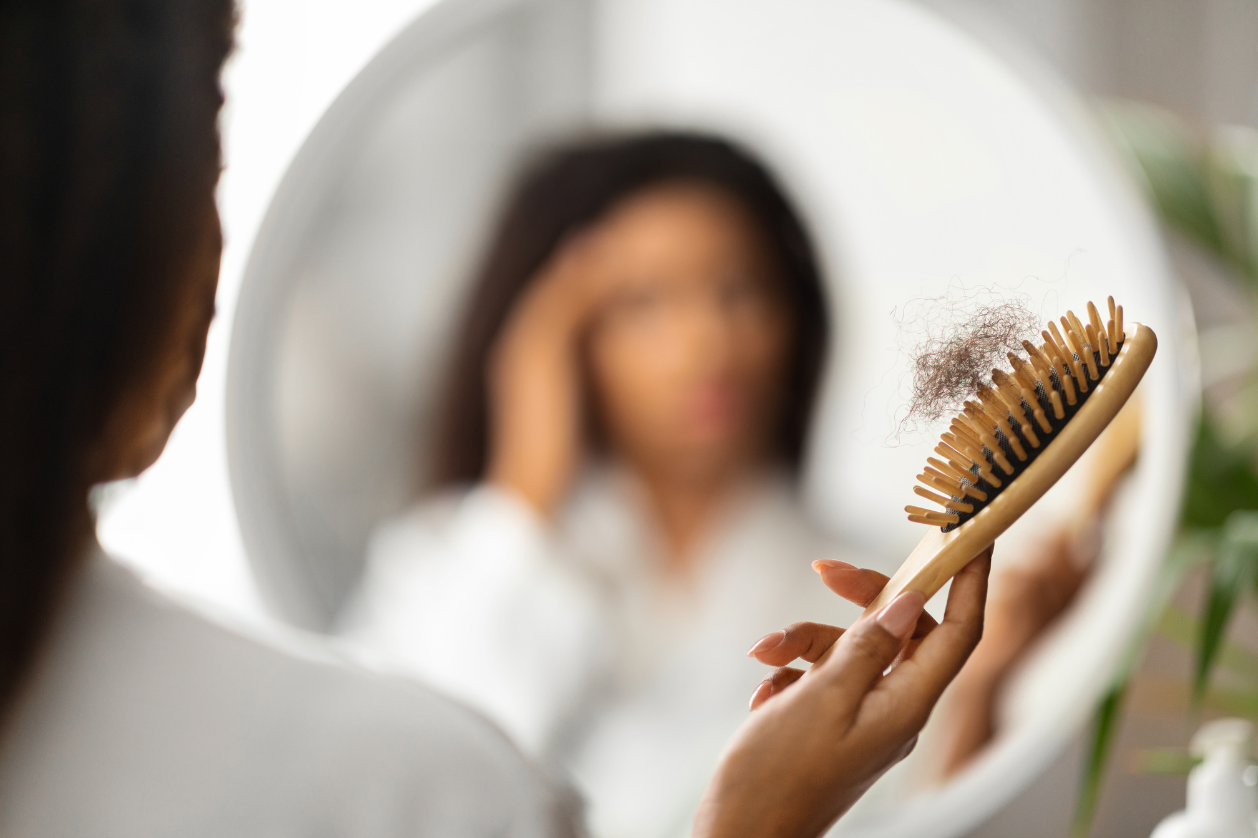 Woman noticing hair shedding in brush while looking in mirror