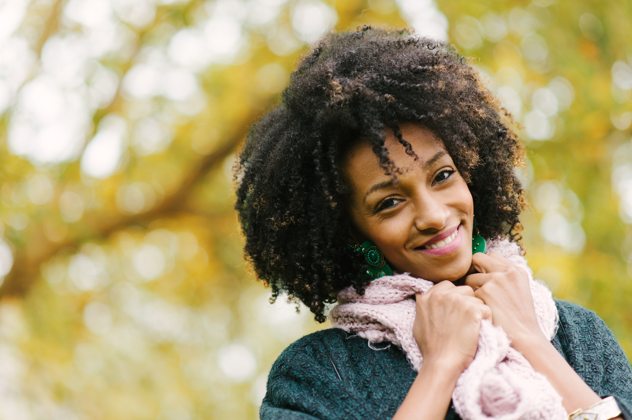 Woman with natural curly hair outdoors in autumn, wearing a scarf and showing healthy, moisturized hair.